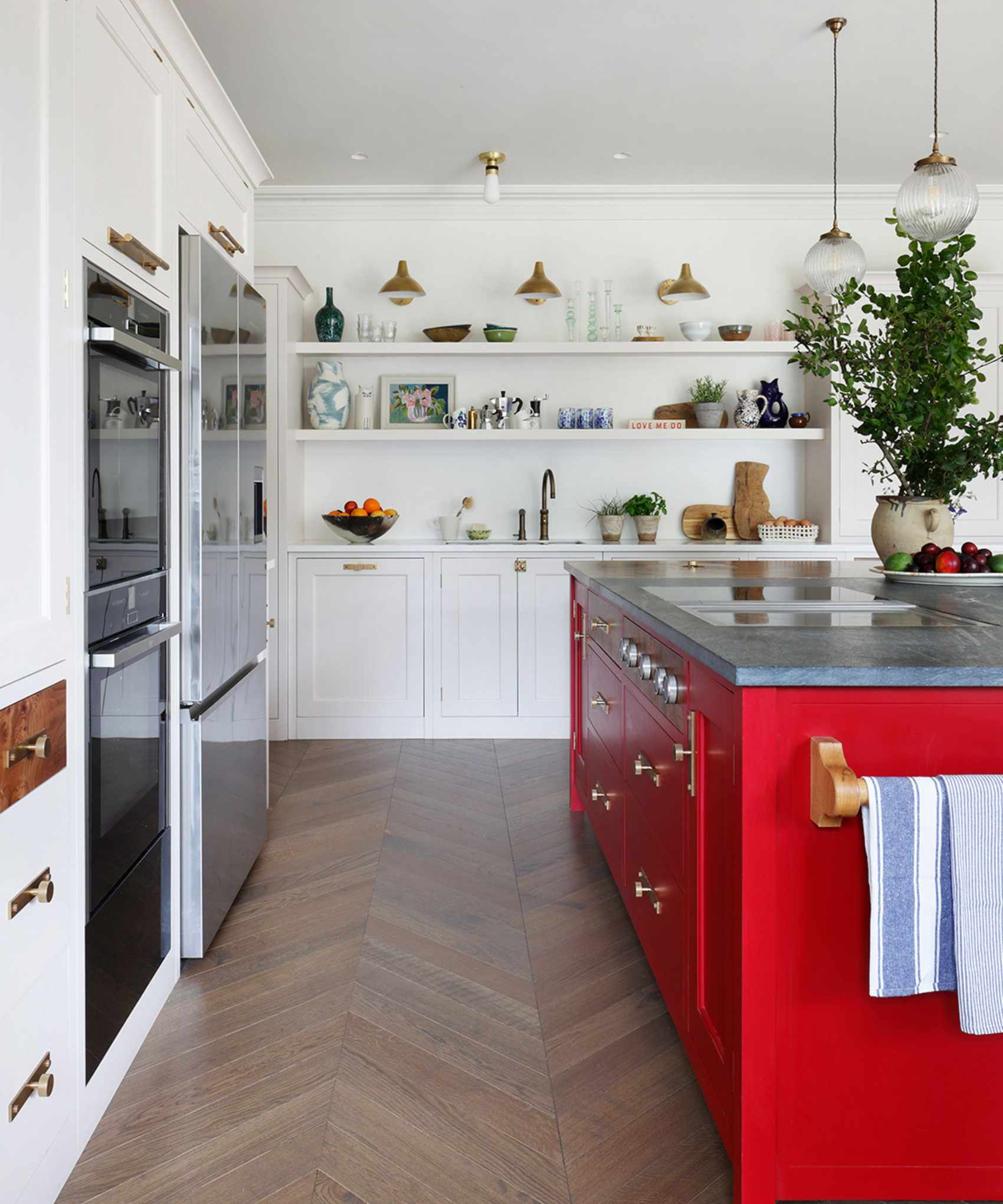 A white kitchen with a red island and brass hardware