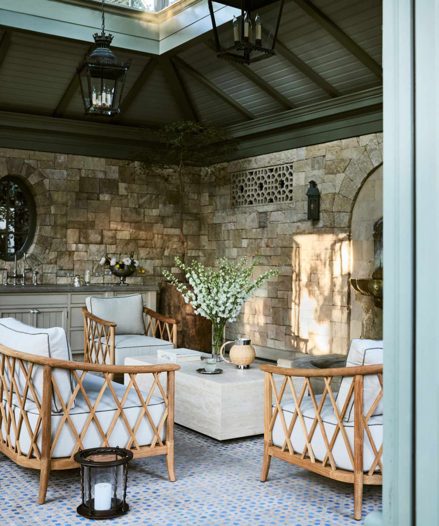 outdoor living room with stone walls and a vaulted green clad ceiling with a rattan seating arrangement with a coffee table and an outdoor bar