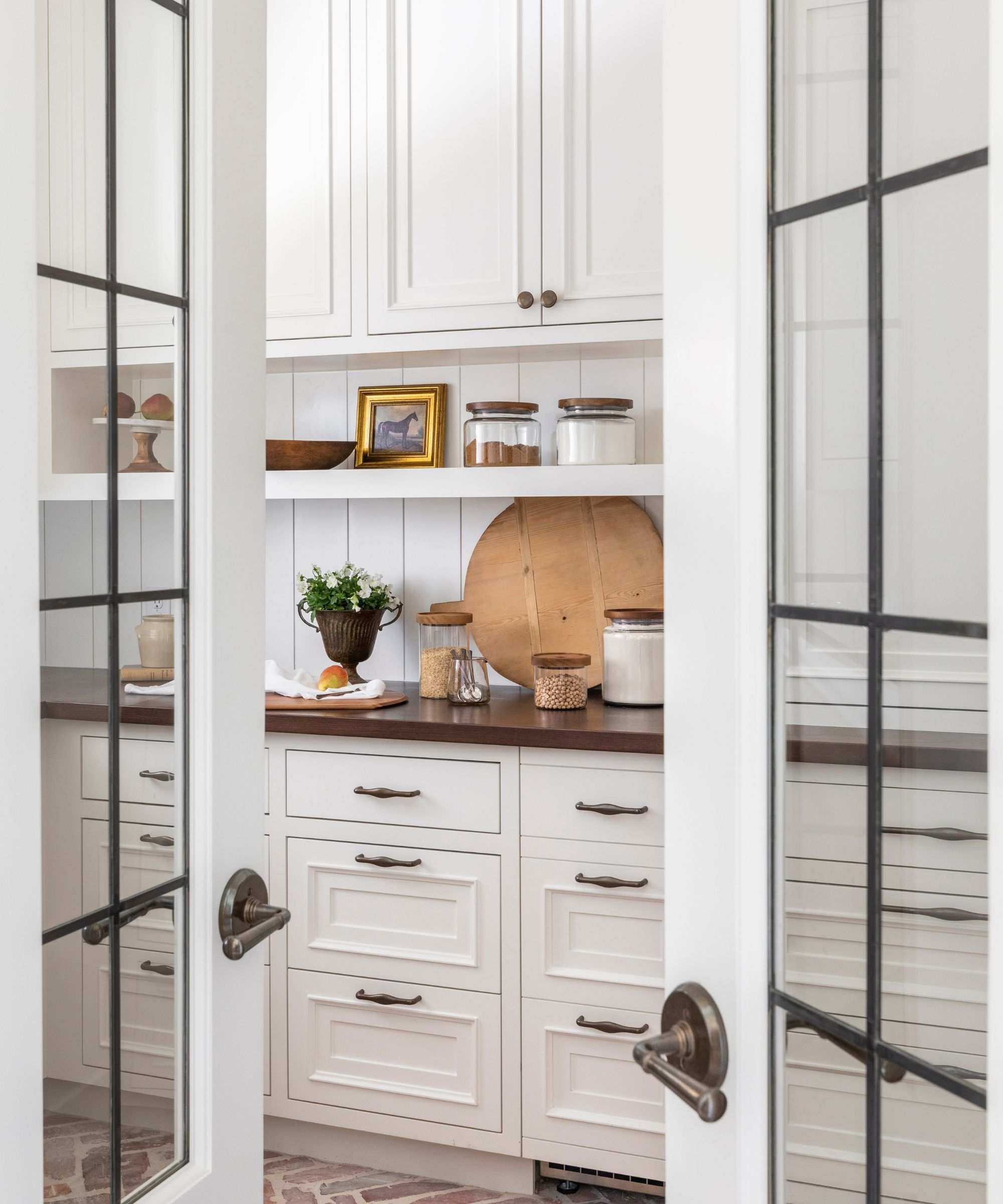 A white pantry with black countertops decorated with a wood cutting board