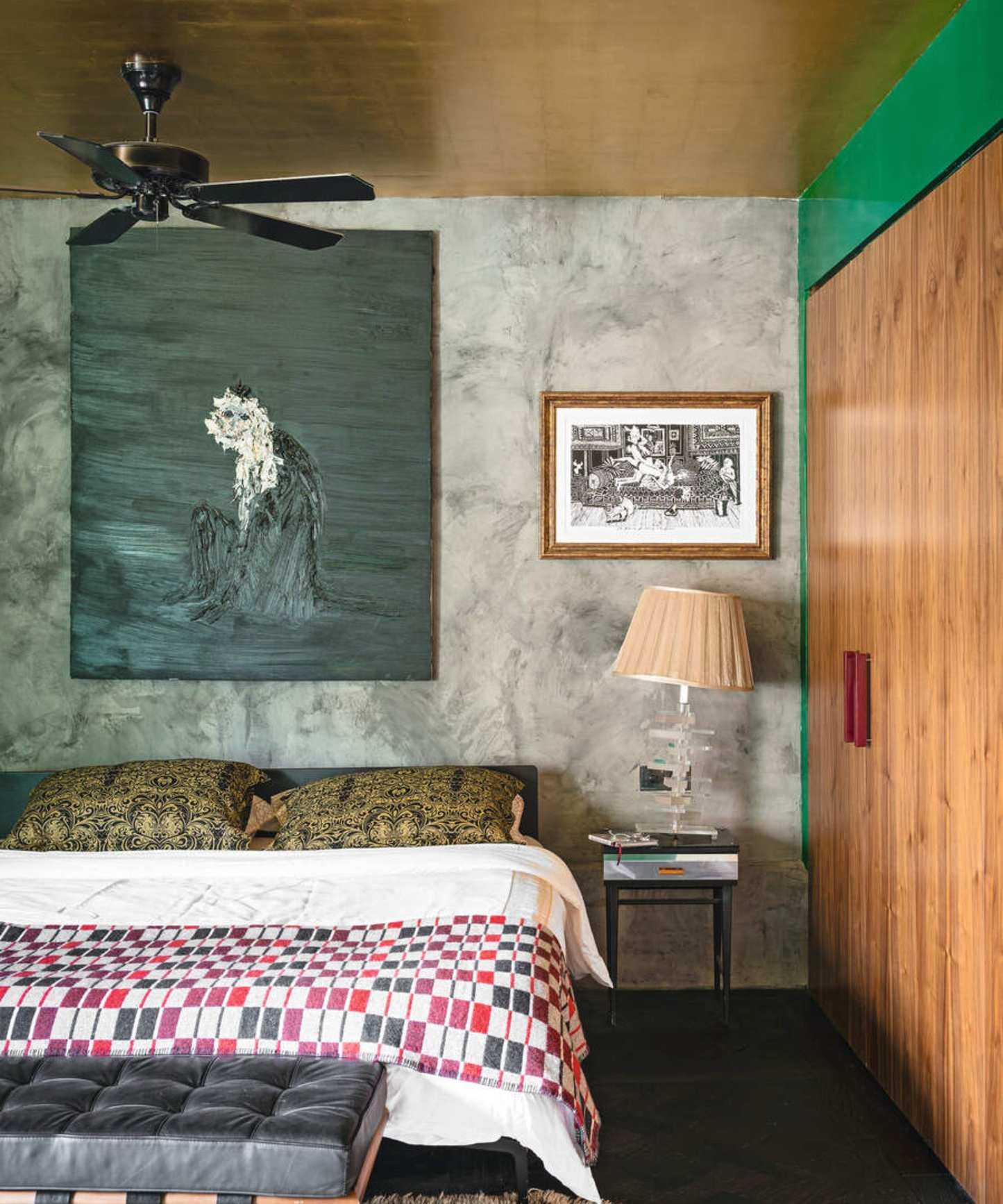 An eclectic bedroom with a gold foil ceiling, a ceiling fan and a large painted canvas above the bed