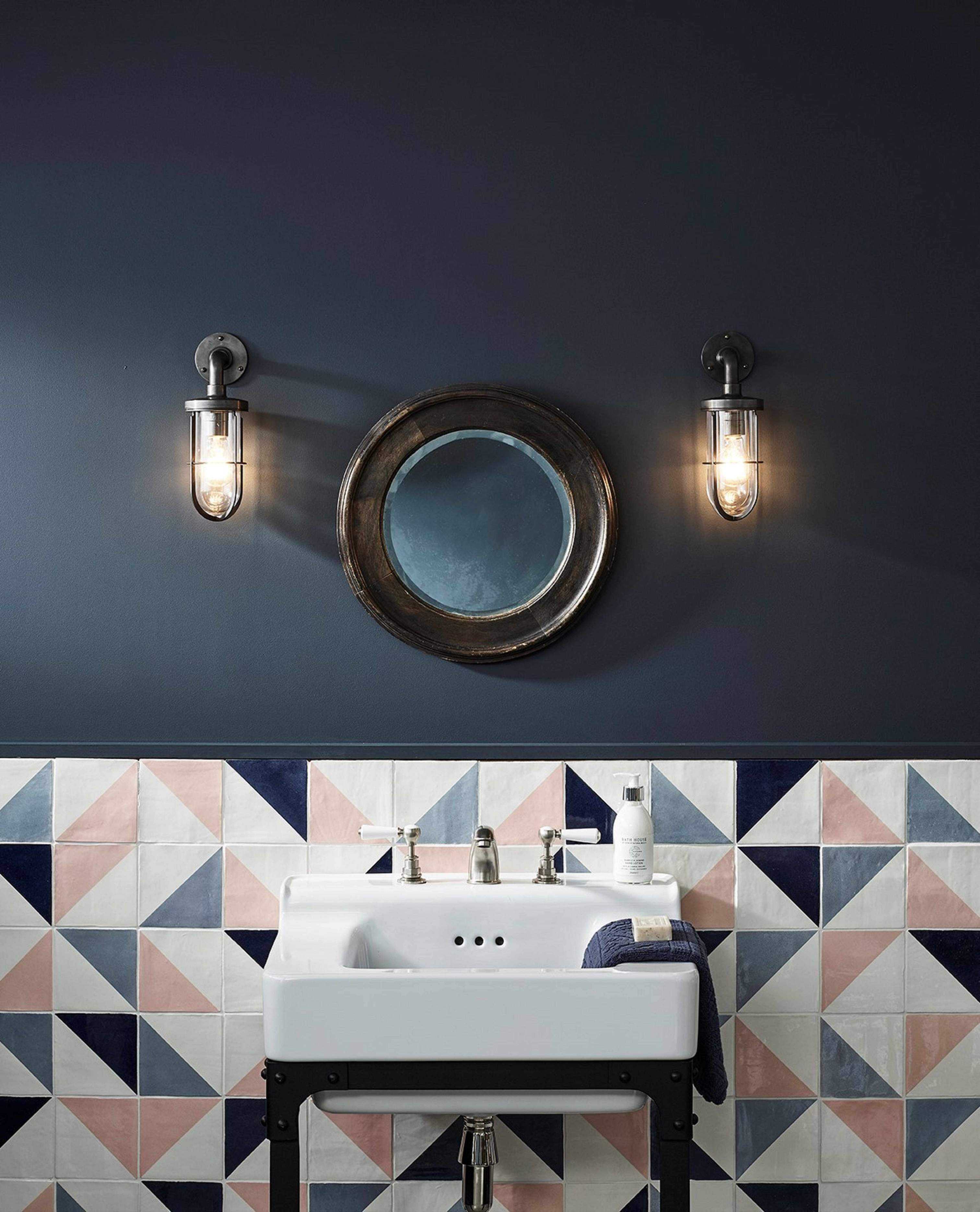 A navy bathroom with a white sink in front of colored wall tiles in blue, pink and white