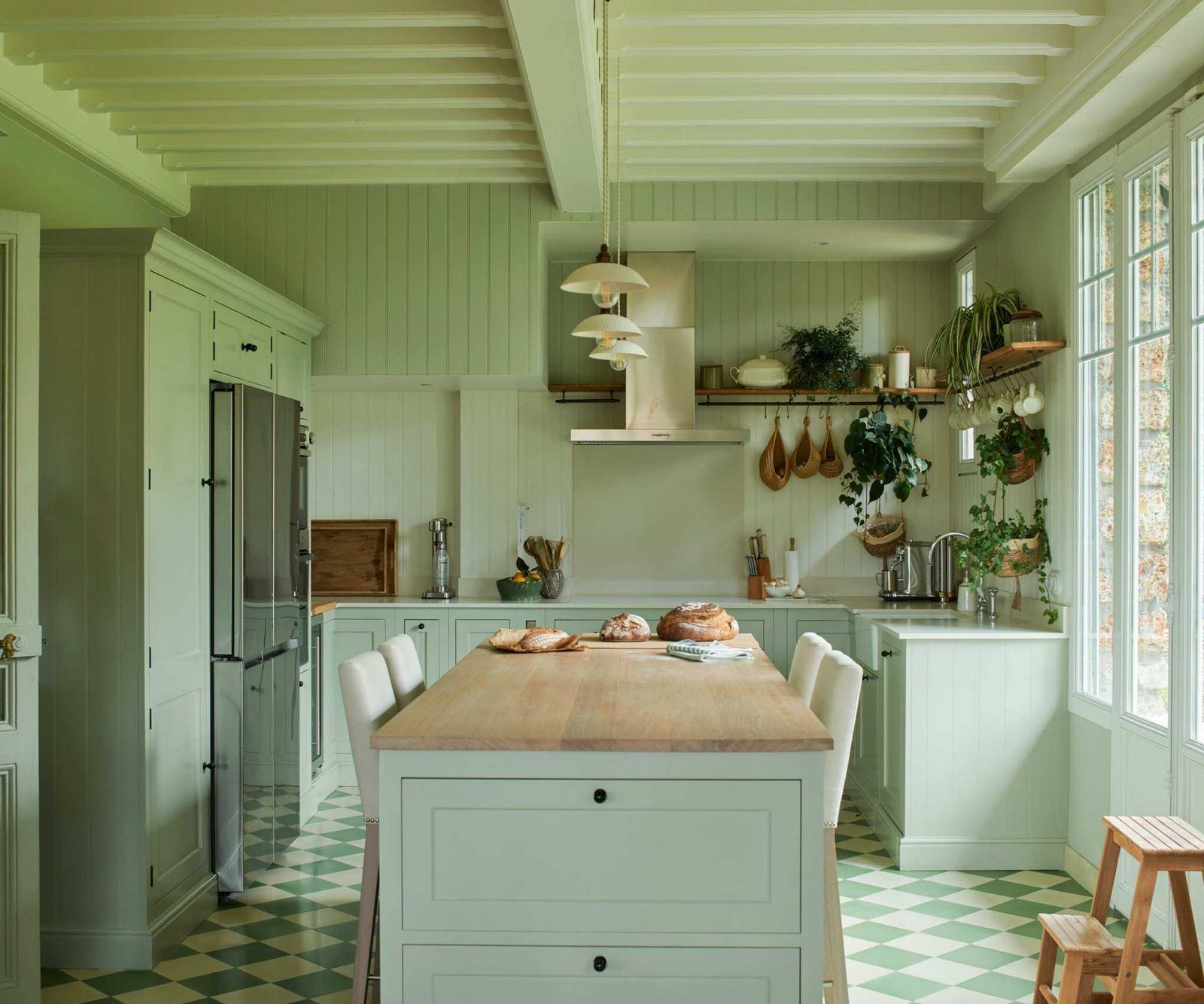 A pale green color-drenched kitchen with a wooden island countertop, a stainless steel range hood, and green and white checkerboard tiled flooring.