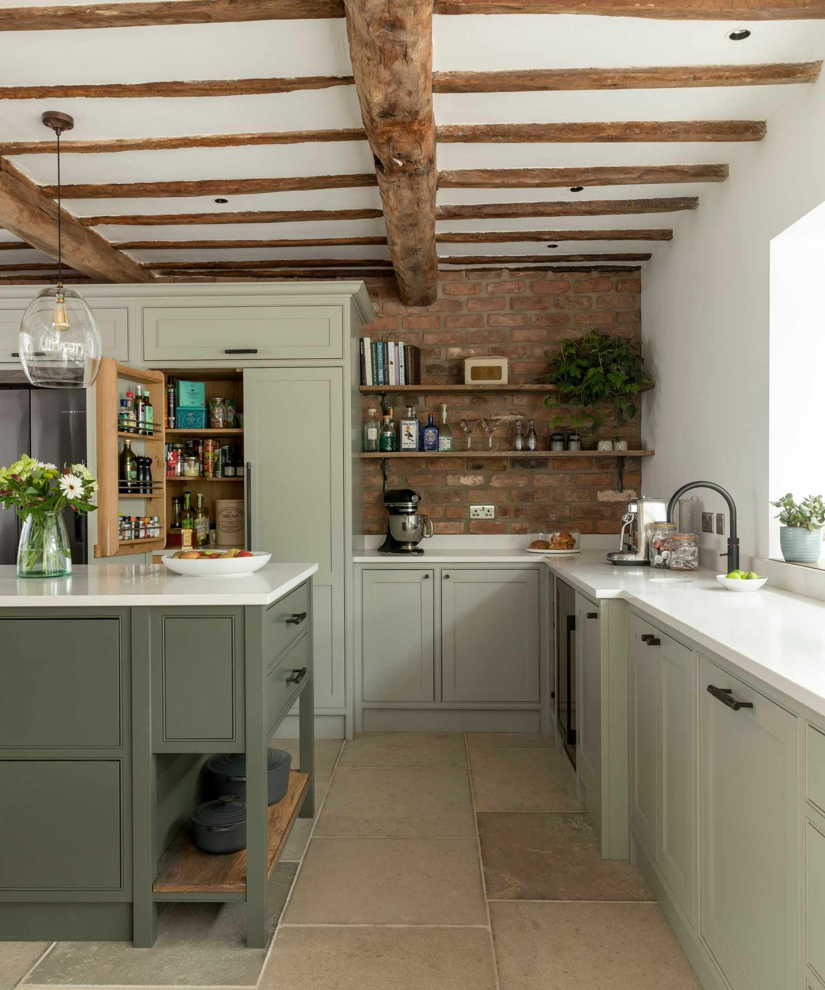 A khaki kitchen island contrasts with a light sage green kitchen in this rustic country kitchen