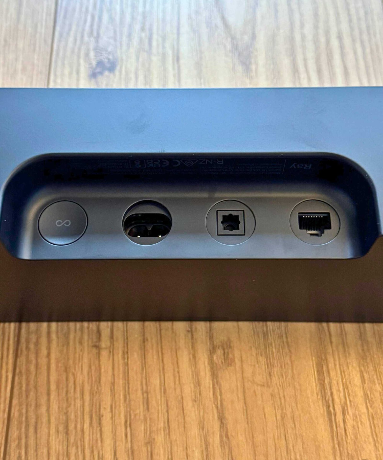 Closeup of the Sonos Ray soundbar's cable ports and button, on wooden floor.