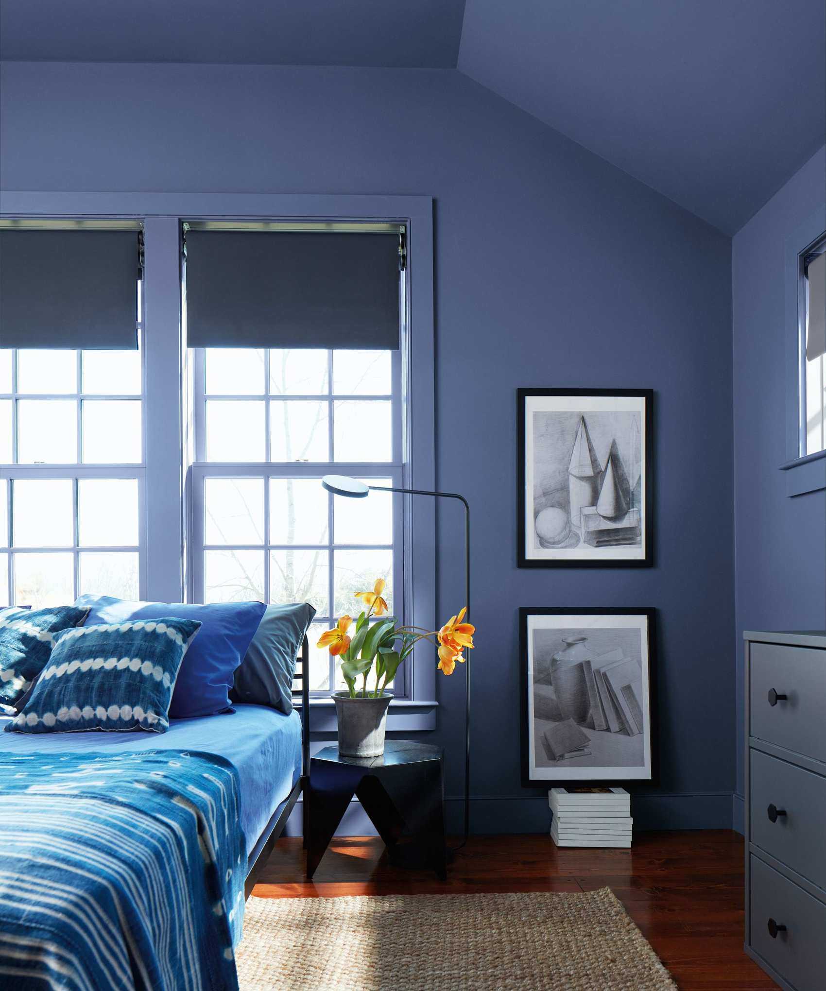Blue bedroom with blue painted walls, blue duvet and pillows on bed, angular bedside table, jute rug and blue drawers