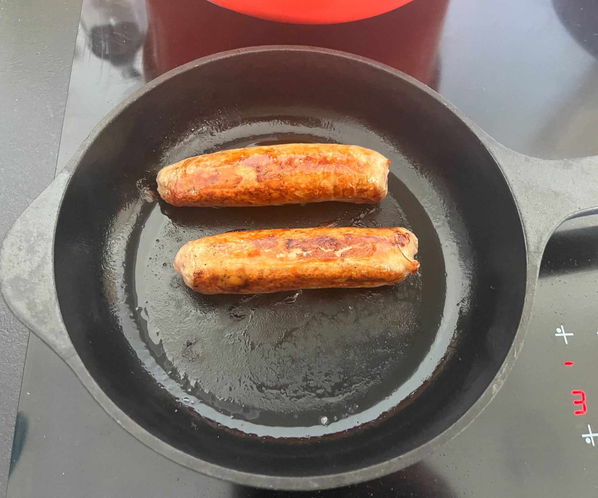 Two golden brown sausages in a small black cast iron skillet