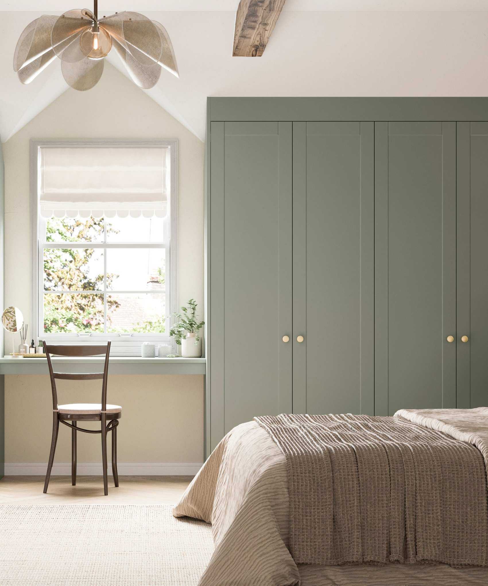 Cream bedroom with carpet, sage green built-in closet and matching vanity table with mid century chair. There is a petal statement ceiling light and bright window showing trees beyond